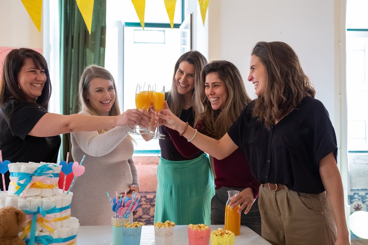 Group of women celebrating a baby shower with orange juice toasts and decorations.